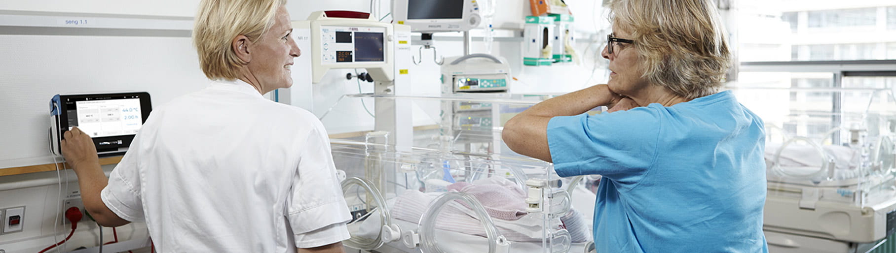 Krankenhaussituation – zwei Pflegekräfte von der Neugeborenenintensivstation verwenden einen transkutanen Monitor von Radiometer